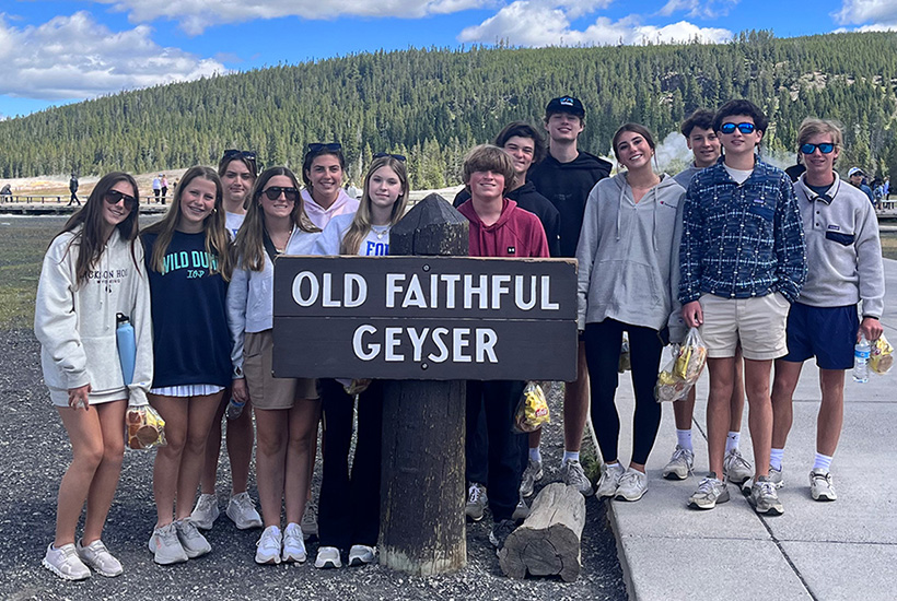 teens at Yellowstone in front of the Old Faithful Geyser sign